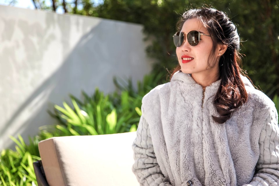 Woman Wearing Gray Fur Coat And Sunglasses Sitting Near Green Leaf Plants