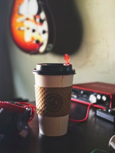 White And Brown Labeled Plastic Coffee Cup On Brown Tabletop Near Black Multimedia Player photo