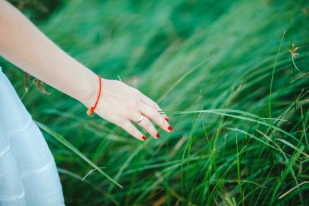 Woman Wearing White Skirt Orange Bracelet And Red Manicure Beside Green Grass