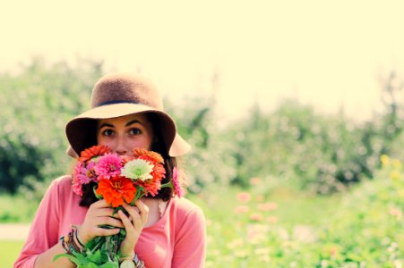 Woman Wearing Hat And Holding Flowers Surrounded By Plants