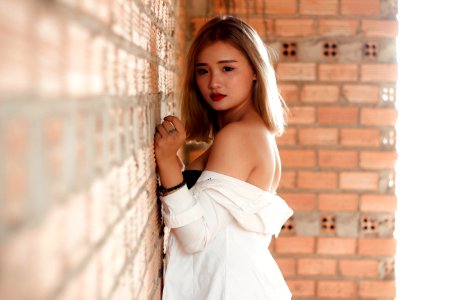 Shallow Focus Photography Of Woman In White Top Beside Red Brick Wall photo
