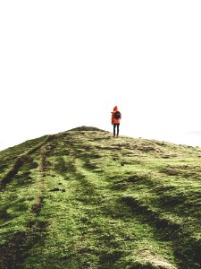 Person Wearing Orange Hoodie Standing On Green Mountain Under White Sky photo