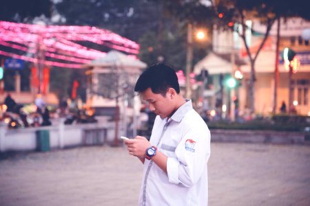 Focus Photography Of Man Wearing White Sports Shirt Holding Smartphone Near Buntings photo
