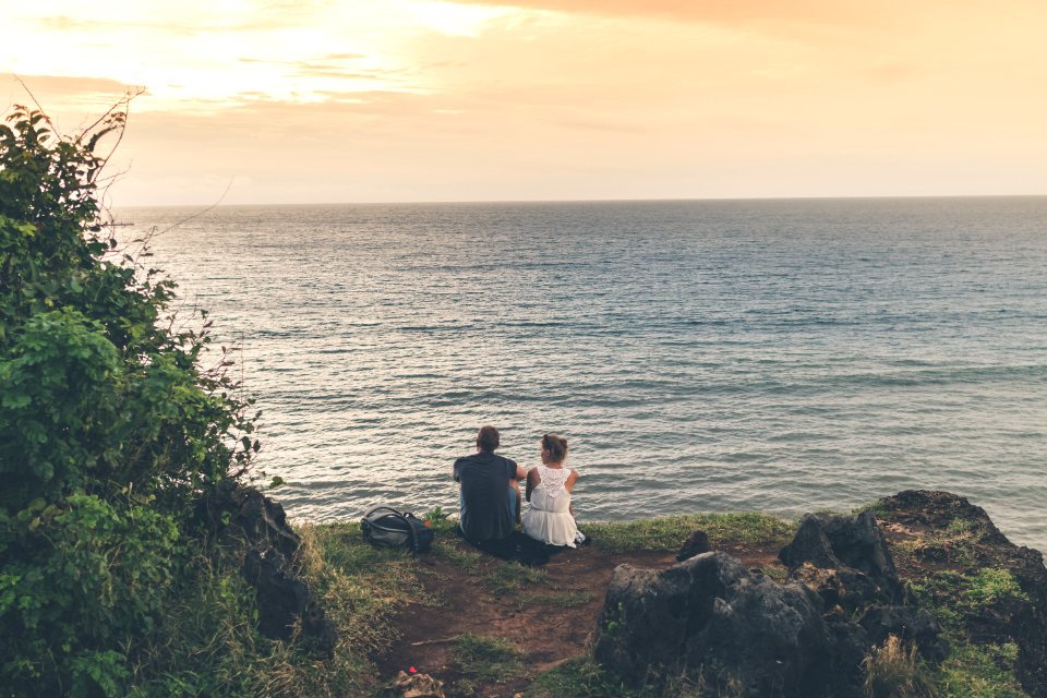 Man And Woman Sitting Near Body Of Water