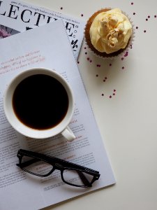 White Ceramic Cup With Coffee On Top Of Opened Book And Near Eyeglasses photo