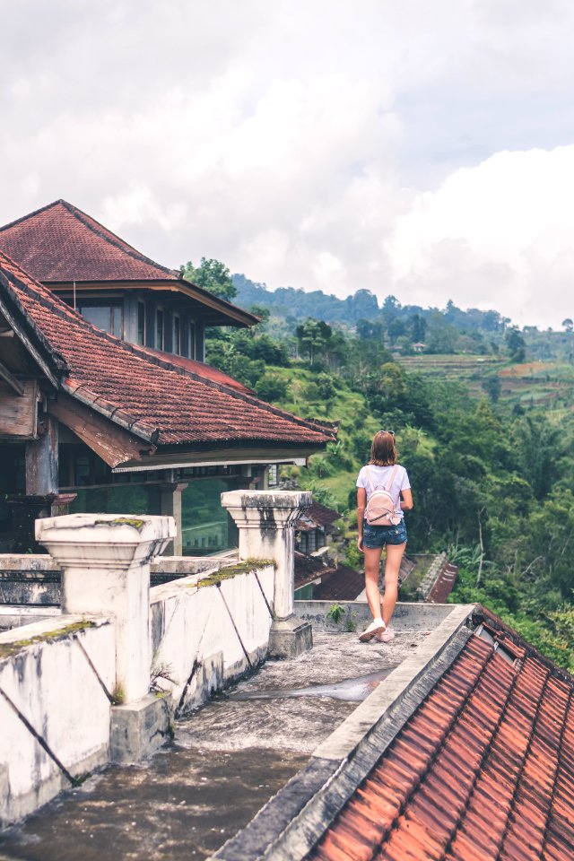 Woman Standing On Gray Concrete Roof Near Mountain Surrounded By Tall Trees