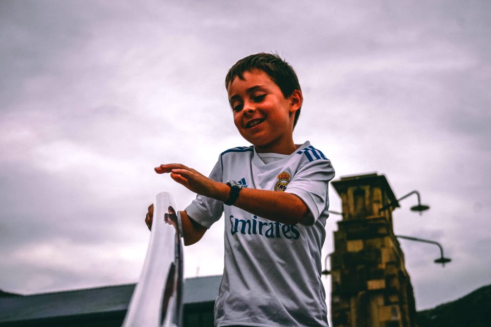 Boy In White And Blue Fly Emirates Jersey Shirt Holding On Stairs Grab Bar Under Gray Skies