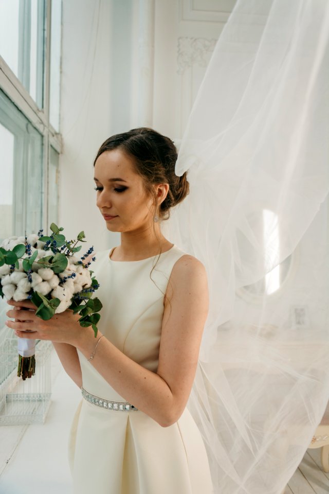 Woman In White Sleeveless Gown Holding White Flower Bouquet Infront Of Window
