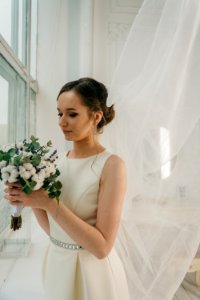 Woman In White Sleeveless Gown Holding White Flower Bouquet Infront Of Window photo