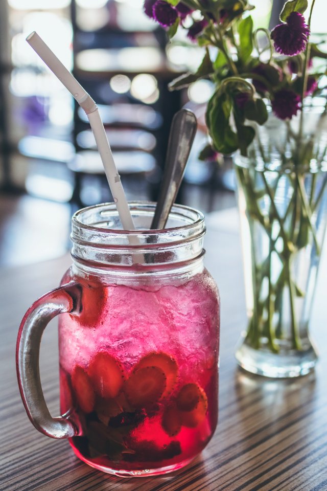 Red Beverage-filled Clear Glass Mason Mug With Straw Beside Purple Flowers In Vase