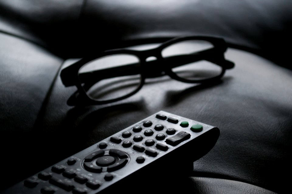 Grayscale Photo Of Remote Control Near Eyeglasses