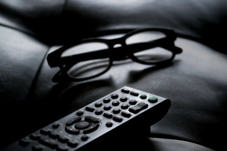 Grayscale Photo Of Remote Control Near Eyeglasses photo