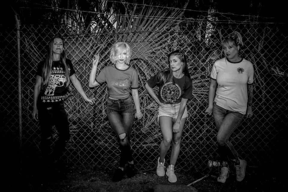 Grayscale Photo Of Four Woman Standing Near On Link Fence photo