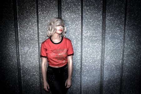 Woman Wearing Red And Black Scoop-neck Shirt And Black Bottoms Leaning On Gray Wall photo