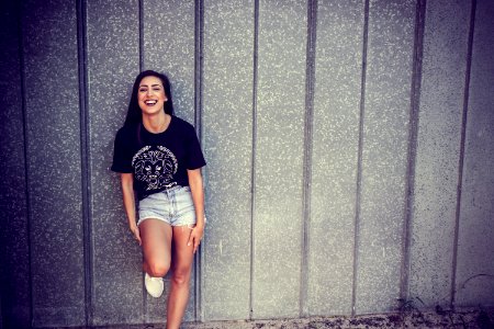 Woman Wearing Black And White Crew-neck T-shirt And Gray Denim Short Shorts Outfit Leaning On Gray Wall