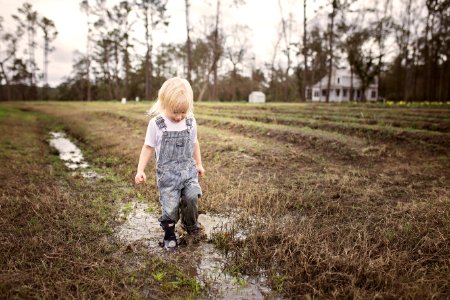 Toddler Wearing Blue Denim Overall Pants Walking On Wet Withered Grass