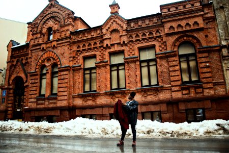 Man Holding Red Coat Standing On Street Near Brown Building