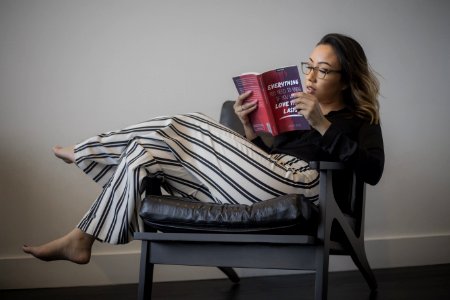 Womens Black Long-sleeved Top White And Black Striped Pants Reading Book Sitting On Gray Wooden Framed Padded Armchair
