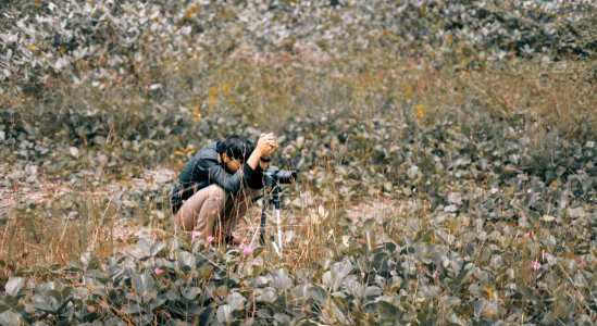 Man Wearing Black Jacket Squatting On Grass Field