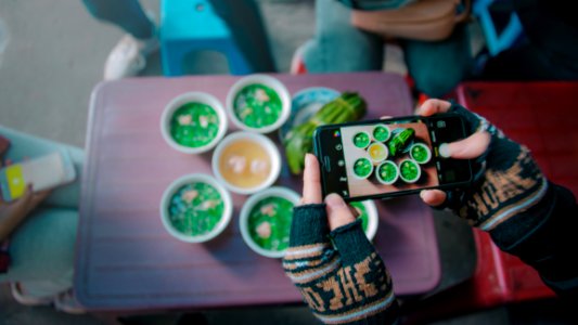 Person Holds Black Iphone Taking Photo Of Round White Ceramic Bowl