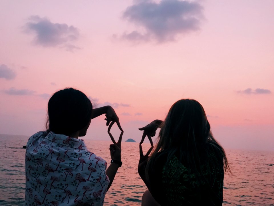 Two Woman Sitting In Front Of Body Of Water