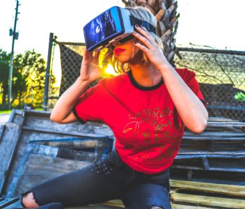Woman Wearing Red And Black Top And Blue Distressed Bottoms Wearing Gray And Black Virtual Reality Sunglasses photo