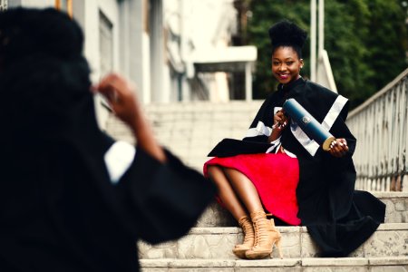 Woman Wearing Black Graduation Coat Sits On Stairs photo