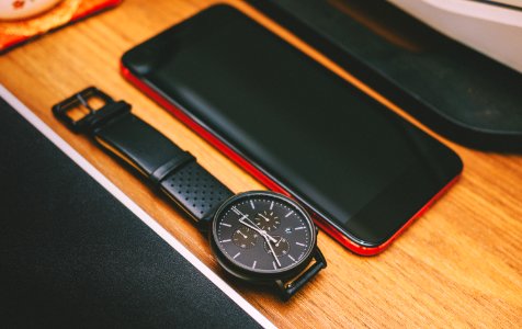 Red Smartphone Beside The Black Chronograph Watch On Brown Wooden Board photo
