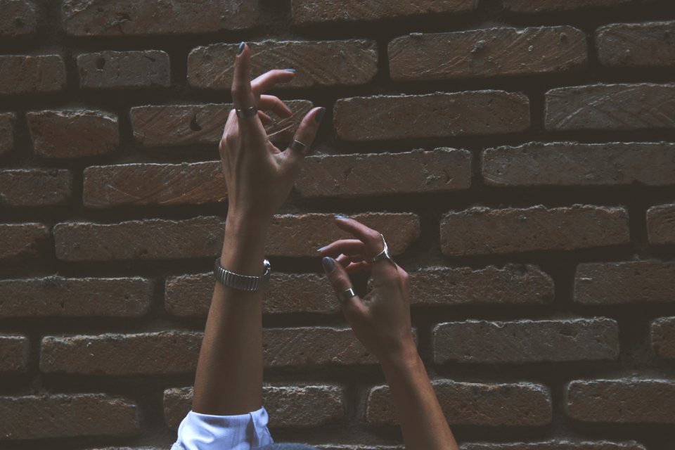 Person Raising Its Two Hand Beside Brown Brick Wall