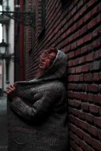 Woman In Orange Sunglasses With Space-dye Cardigan With Hoodie Leaning On Wall Brick