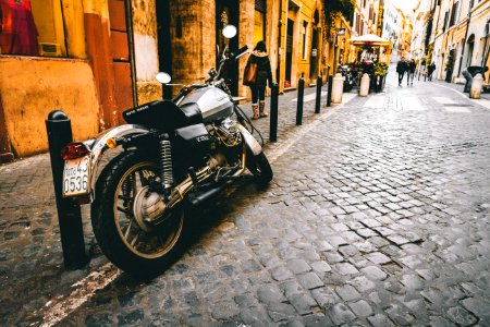 Photograph Of Motorcycle Parked Beside Park Bars Near Woman Walking Through Street photo