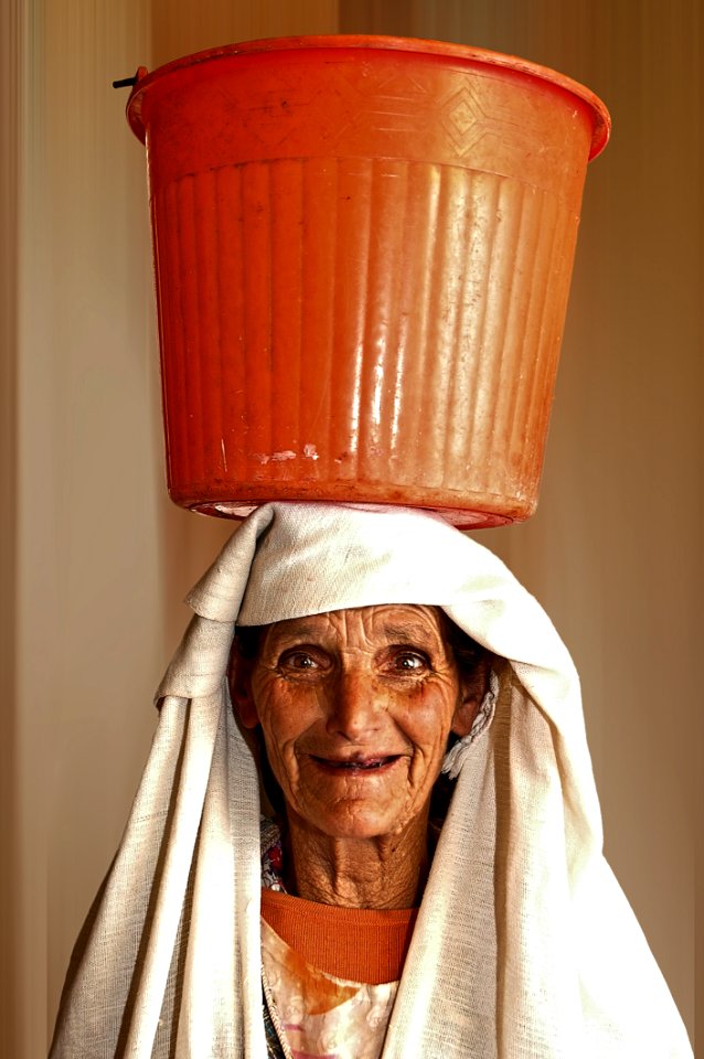 Portrait Photo Of Woman Carrying Orange Plastic Pail On Head
