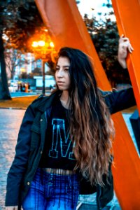 Woman Wearing Black Jacket Leaning On Orange Metal photo