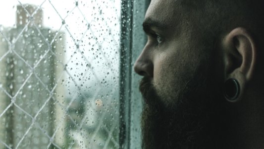 Selective Focus Photography Of Man Staring On Glass Window Filled With Droplets