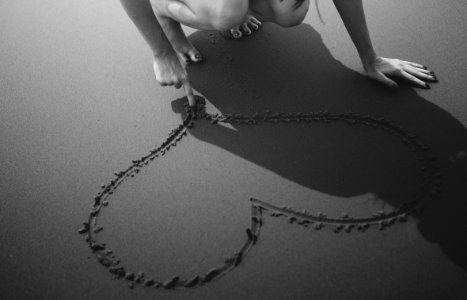 Grayscale Photo Of Woman Drawing Heart On Sand photo