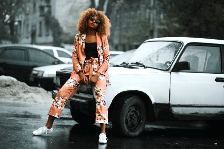 Woman In Pink-and-white Floral Jacket And Pants Sitting On Hood Of Car photo