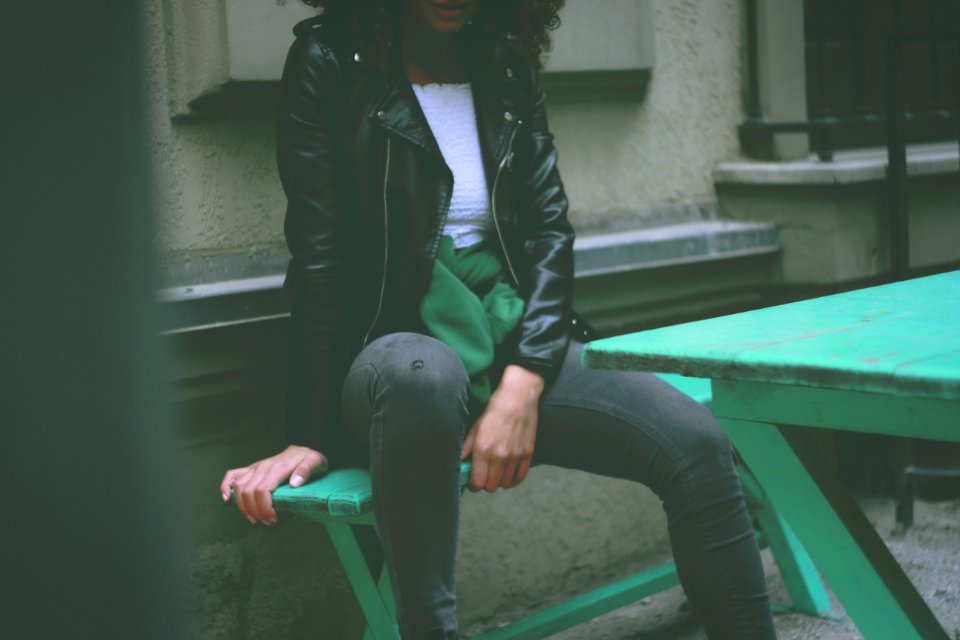 Woman Wearing Black Leather Jacket Sitting On Green Wooden Bench