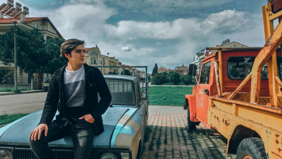 Man In Black Zip-up Jacket On Blue Car Beside Orange Truck photo