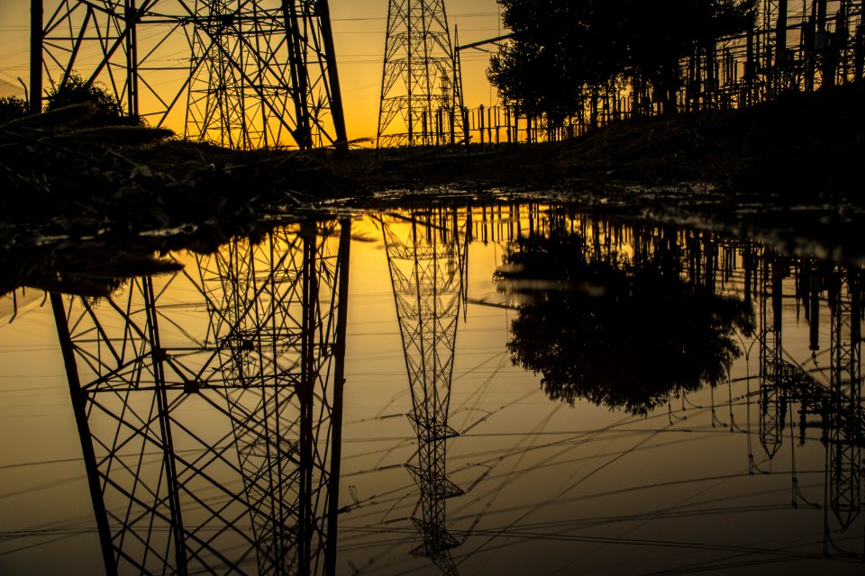 Silhouette Of Trees And Electric Tower Reflecting On Body Of Water During Sunset