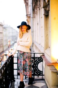 Pregnant Woman Wearing White Sweater And Multicolored Floral Skirt Standing On Balcony