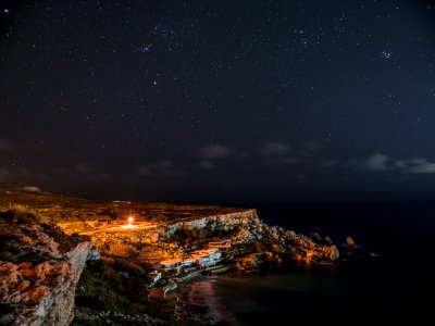 Rock Cliff Near Body Of Water Under Clouds And Sky During Nighttime