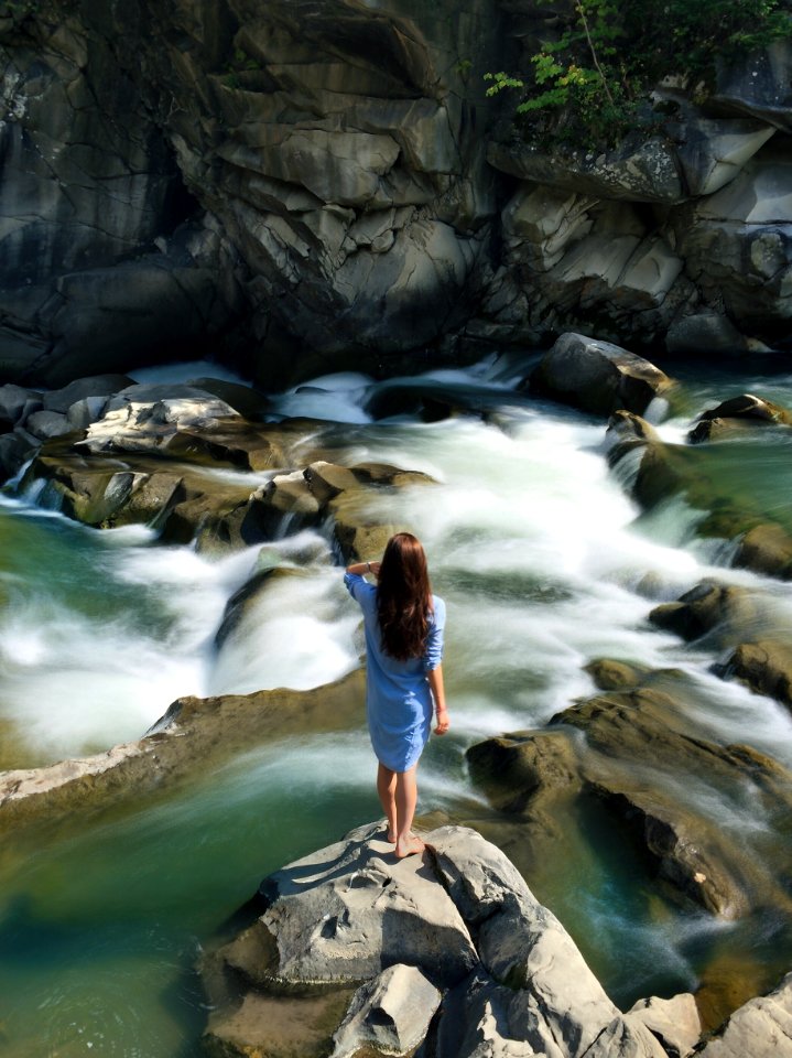 Woman In Blue Long-sleeved Dress Standing In Middle Of Rock With Raging Water photo