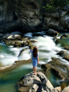 Woman In Blue Long-sleeved Dress Standing In Middle Of Rock With Raging Water