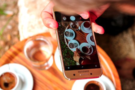 Person Holding A Samsung Galaxy Smartphone Taking A Picture On Their Coffees photo