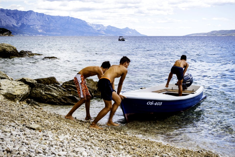 Three Men Pushing Speed Boat On Seashore