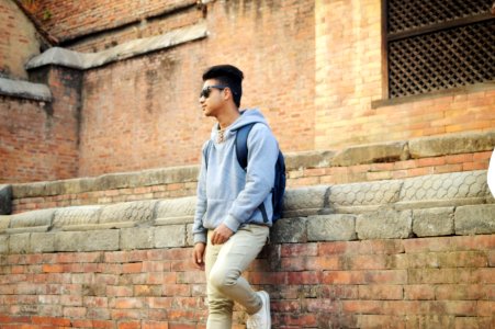Man In Heather-grey Pullover Hoodie And Beige Pants Standing Near Brick Wall photo