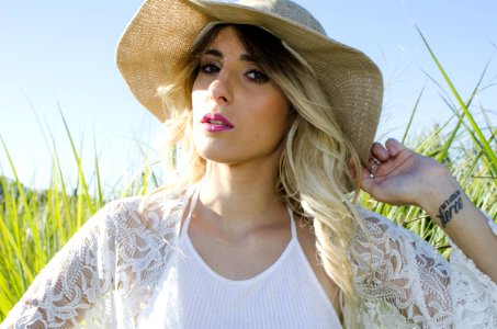Woman Wearing Brown Hat And White Cardigan Standing In Middle Of Grass Field photo