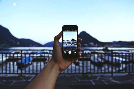 Person Holding Iphone Taking Picture Of Mountain Near Body Of Water photo