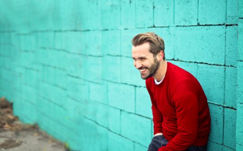 Man Wearing A Red Sweater Leaning On A Blue Wall photo