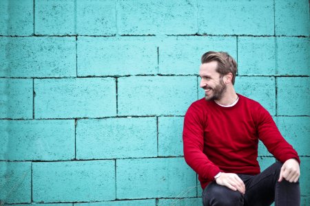 Man Wearing Red Sweatshirt And Black Pants Leaning On The Wall photo